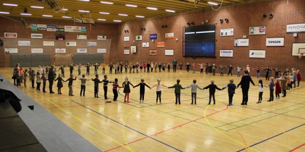 0-klasser i stor ring med hinanden i hånden i HEI-hallen på 100-dages-festdagen efter første 100 dage i skole