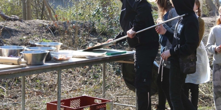 En voksen og nogle elever anonyme står ved udendørs bord i Klub Skæring og bager pizza
