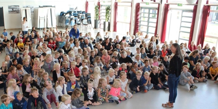 Festsalen lidt fra oven, fuld af små elever med Anne Schwartz stående foran dem.